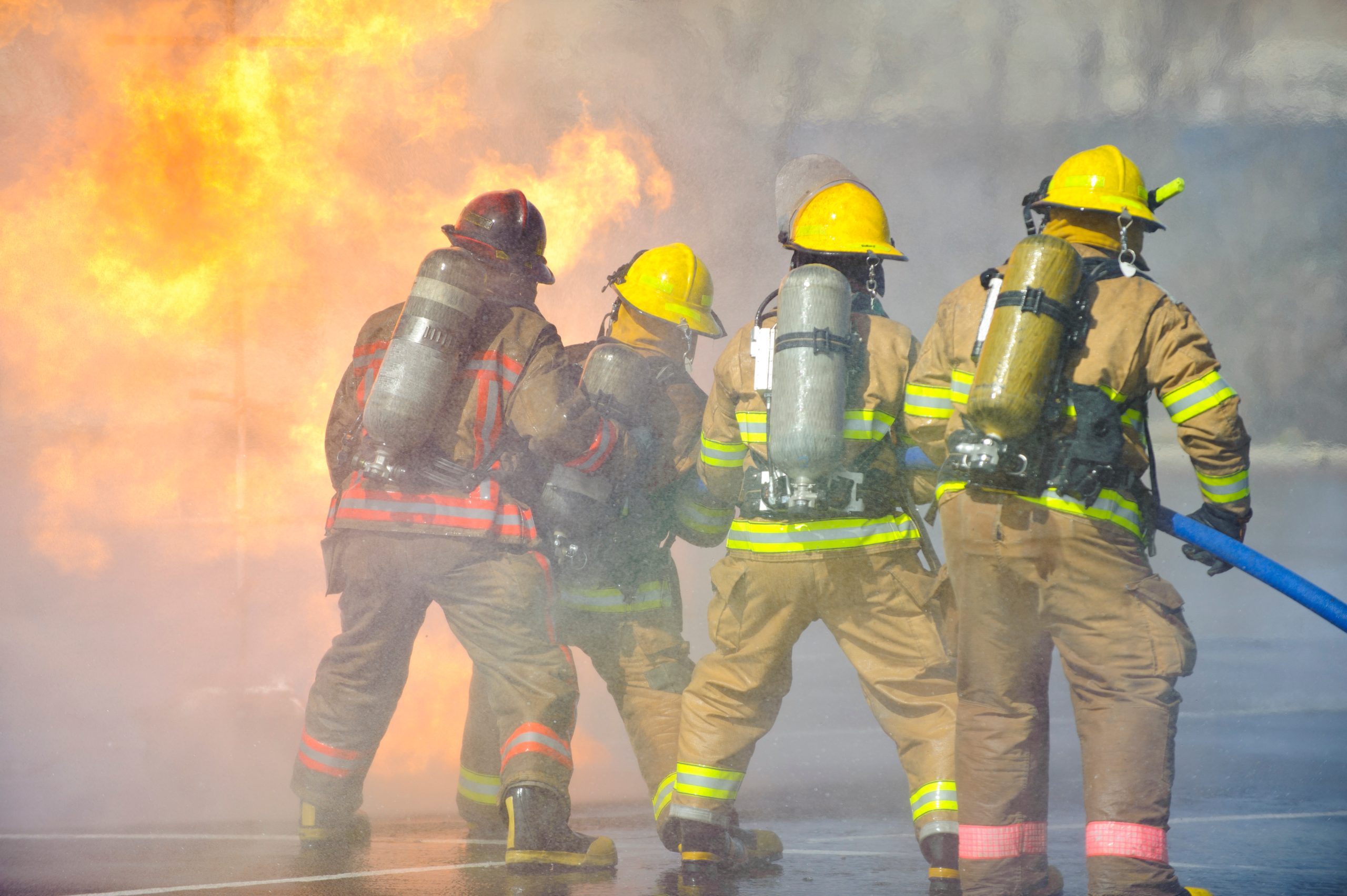 Directed by an officer in a red helmet, firefighters attack a propane fire during a training exercise.